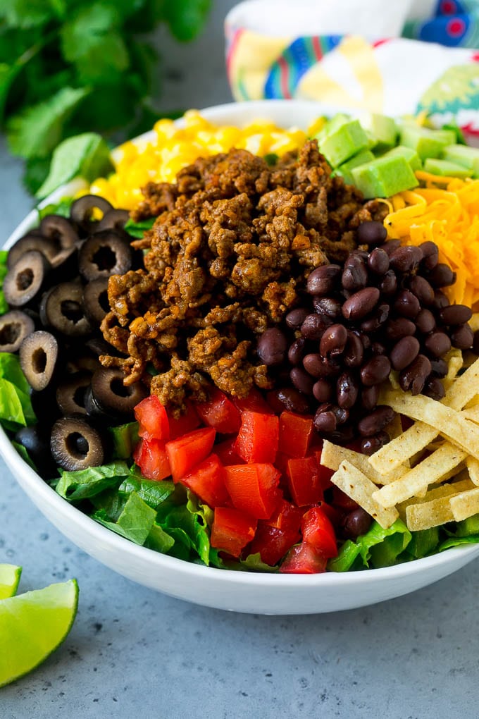 Ground beef, tortilla strips, beans, tomatoes, olives, corn and avocado over lettuce.