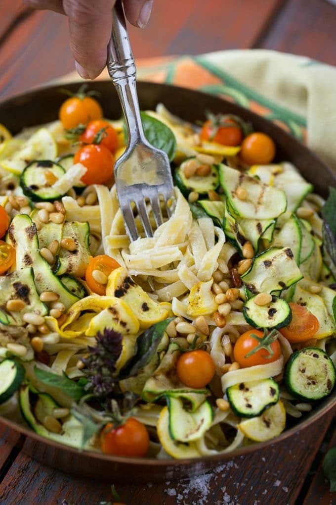 A fork in a bowl of zucchini fettuccine Alfredo pasta.