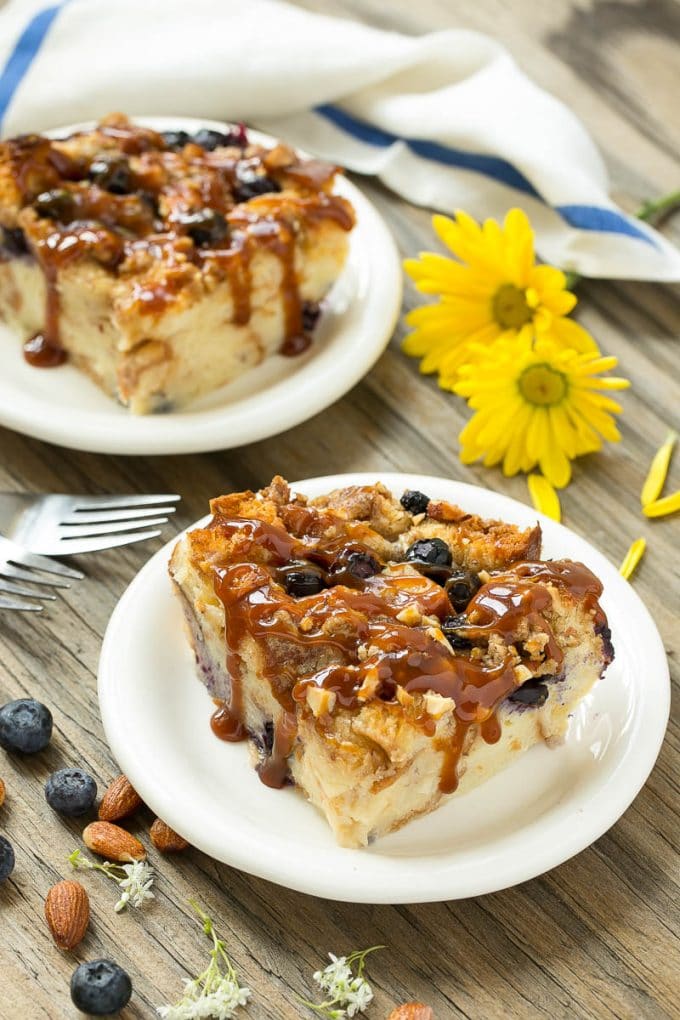 Two pieces of blueberry bread pudding on plates with salted caramel on top.