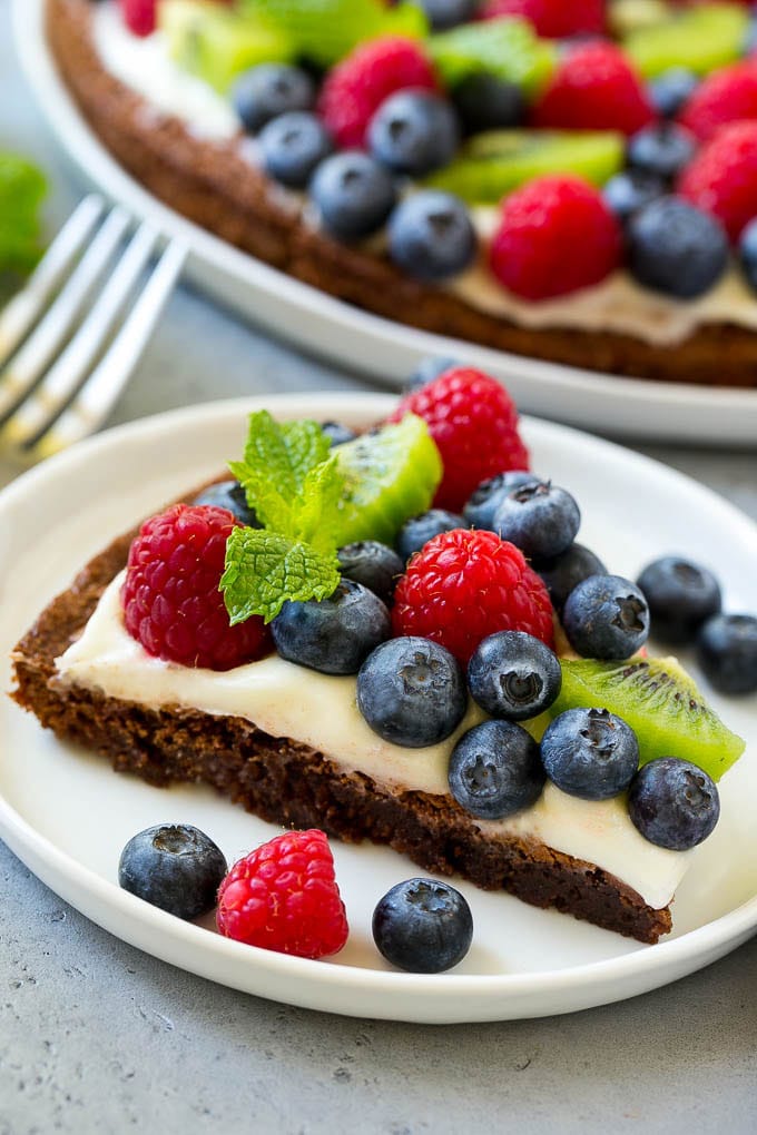 A slice of brownie pizza on a plate, topped with fruit.