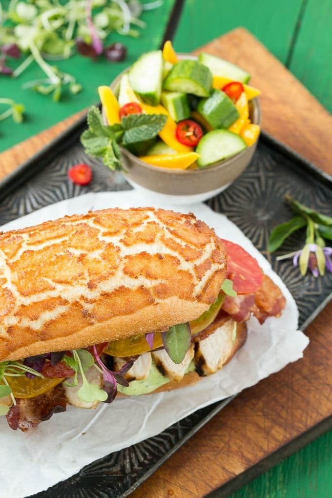 A chicken sandwich with a bowl of mango cucumber salad on the side.