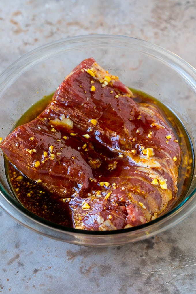 Raw flank steak in a bowl of marinade.