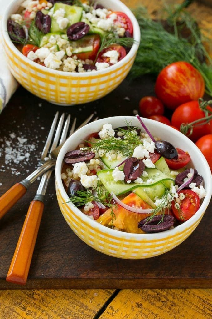 Two bowls of Greek couscous with sliced tomatoes, red onion and fresh dill.