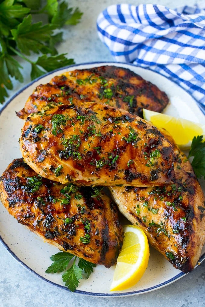 A platter of grilled chicken breast served with parsley and lemon.