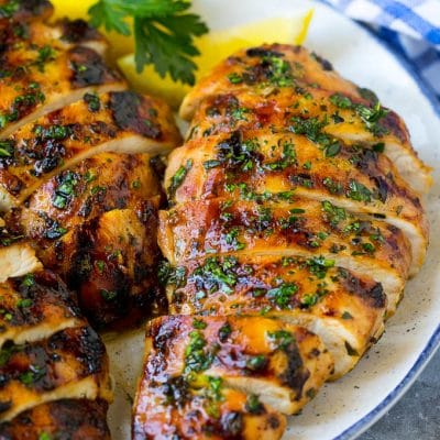 Sliced grilled chicken breast garnished with herbs and lemon.