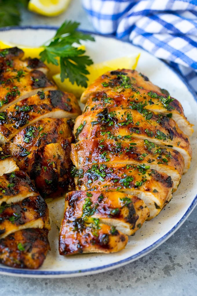 Sliced grilled chicken breast garnished with herbs and lemon.