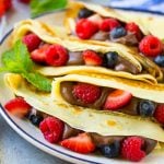 A plate of four crepes that are filled with nutella, strawberries, blueberries and raspberries.