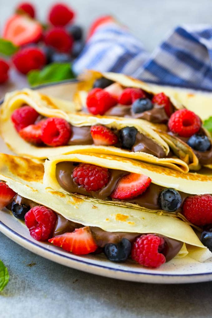 A stack of crepes that are stuffed full of chocolate Nutella spread and fresh berries.