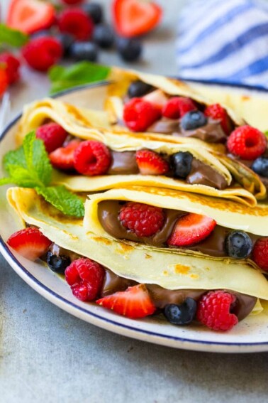 A plate of four crepes that are filled with nutella, strawberries, blueberries and raspberries.