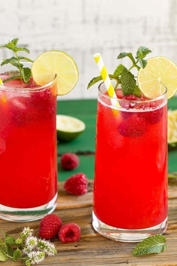 Glasses of raspberry limeade garnished with mint and limes.