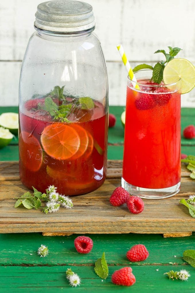 A jug and glass of raspberry limeade sitting on a wooden board.