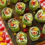 Veggie pinwheels on a board filled with bell peppers, carrots, cabbage and spinach.