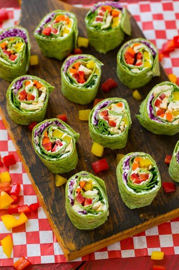 Veggie pinwheels on a board filled with bell peppers, carrots, cabbage and spinach.