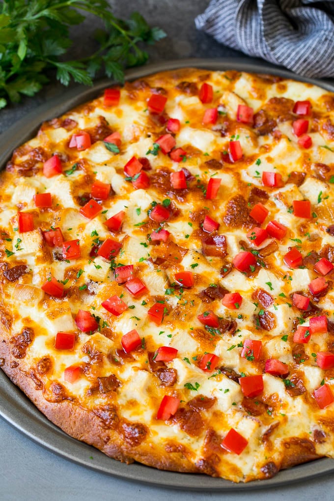 A pizza topped with chicken, bacon, tomatoes and parsley.