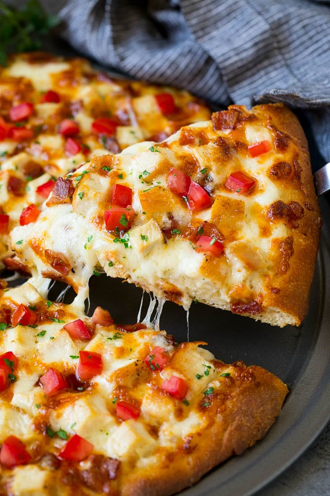 A slice of chicken Alfredo pizza with bacon and fresh tomatoes.