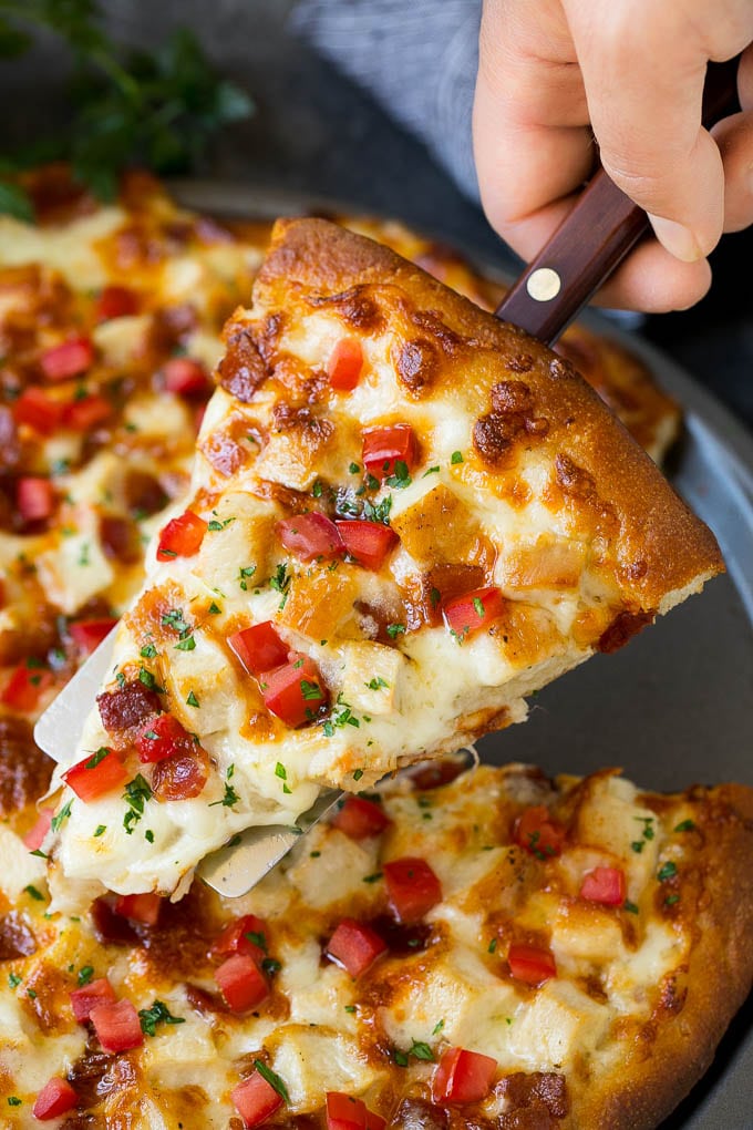 A hand holding a spatula with a piece of chicken Alfredo pizza on it.