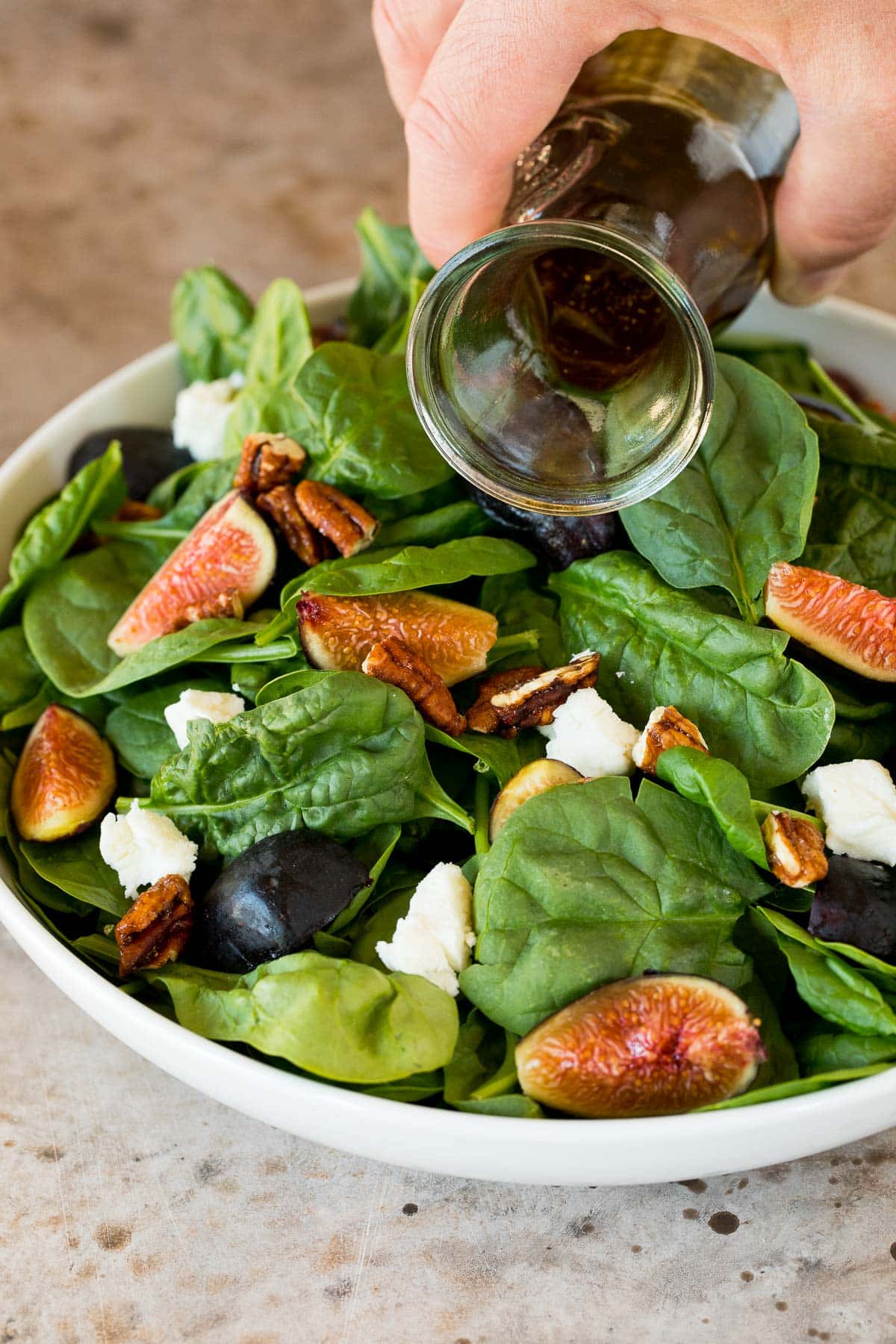 Dressing being poured over spinach salad.