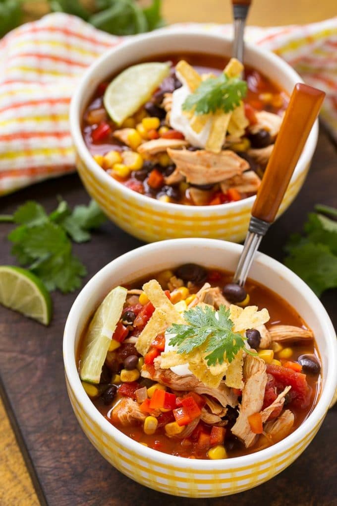 Two bowls with toppings like tortilla strips, cilantro and lime wedges.