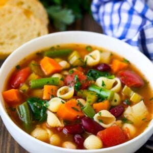 A bowl of minestrone soup made with vegetables and beans, served with a side of bread.
