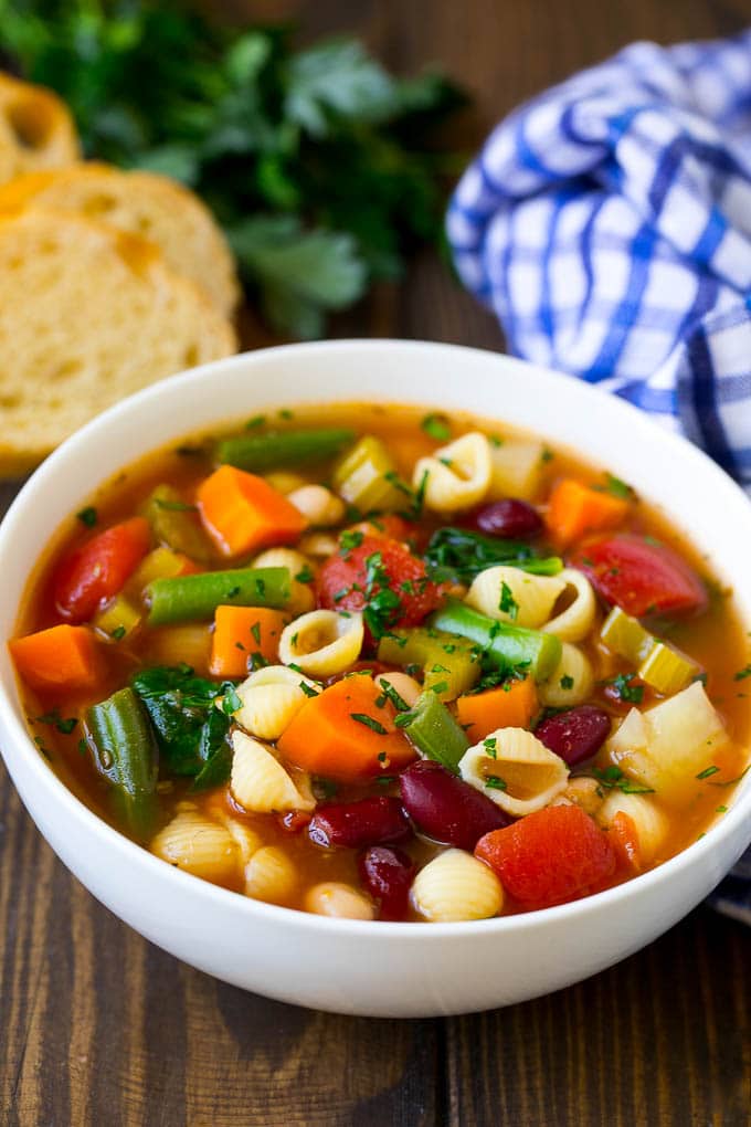 A bowl of minestrone soup made with vegetables and beans, served with a side of bread.