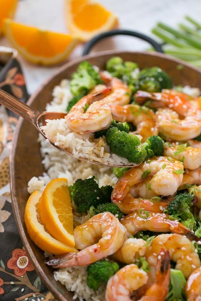 A spoon serving up a portion of steamed rice with stir fry on top.