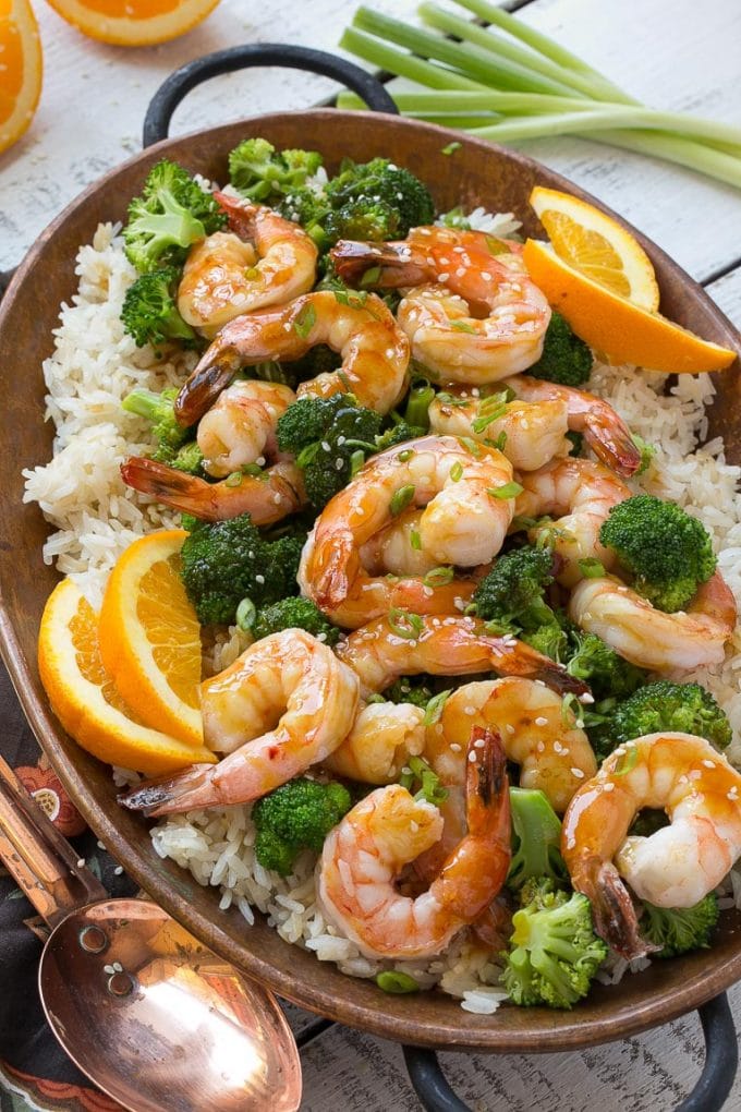 Shrimp and broccoli garnished with sesame seeds and green onions in a pan of rice.