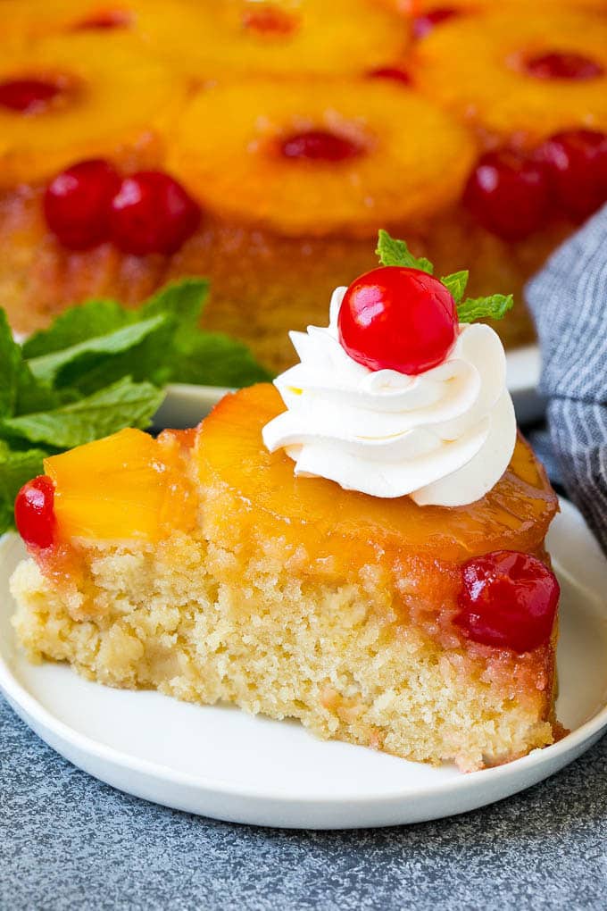 A slice of pineapple upside down cake topped with whipped cream and a cherry.