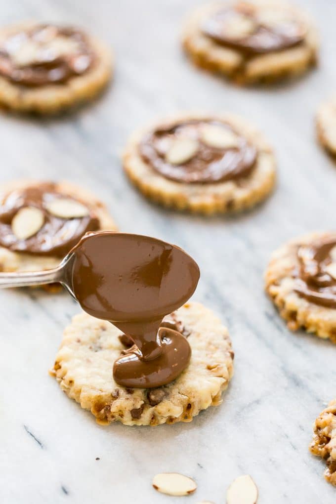 A spoon pouring melted chocolate onto a cookie.