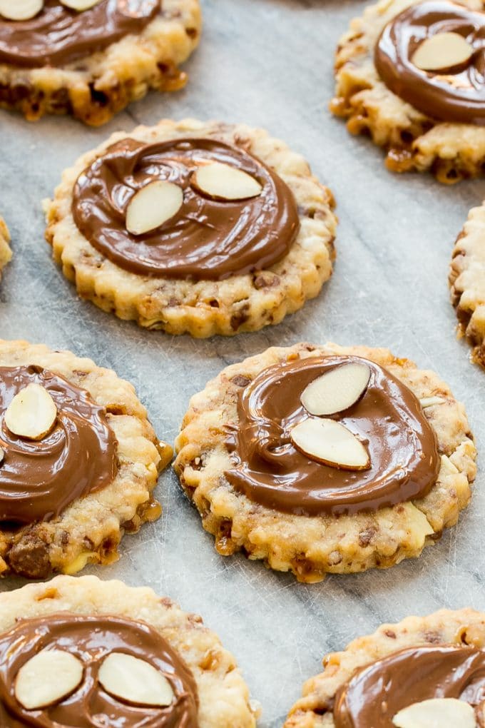 Almond roca cookies on a slab of marble topped with chocolate and almonds.