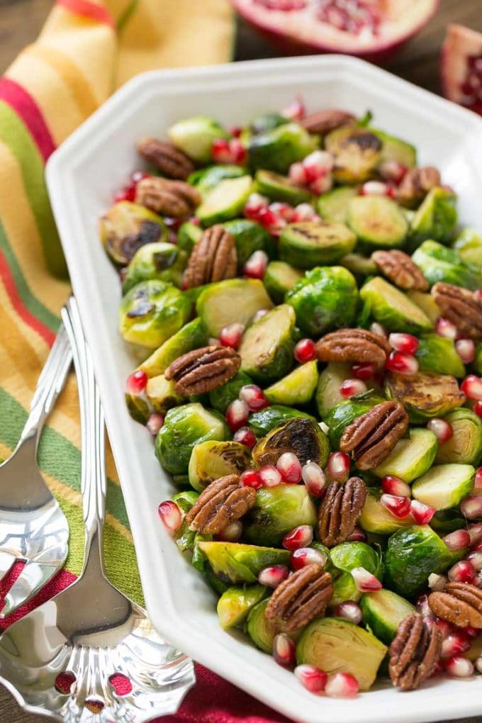 Cooked sprouts in a serving dish with serving utensils next to them.