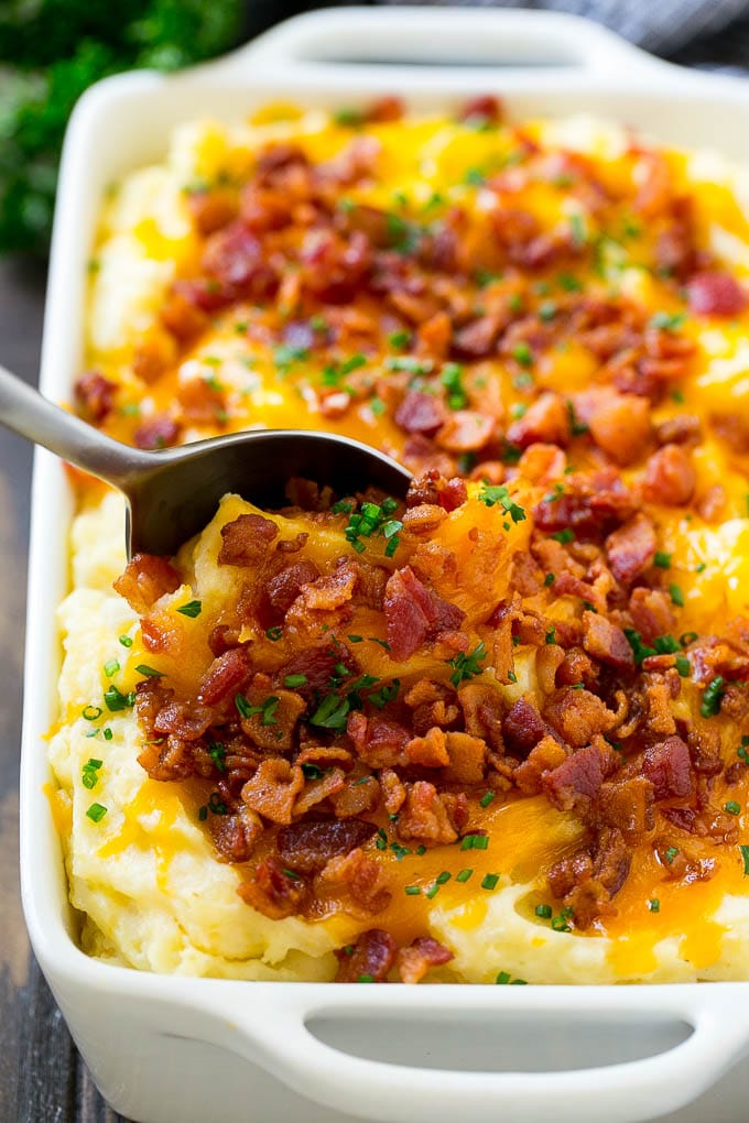 A dish of loaded mashed potato casserole with a serving spoon in it.
