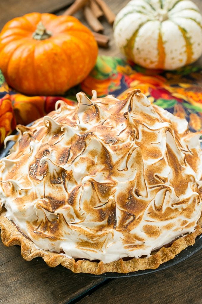 A pumpkin pie with meringue topping served alongside fresh decorative pumpkins.