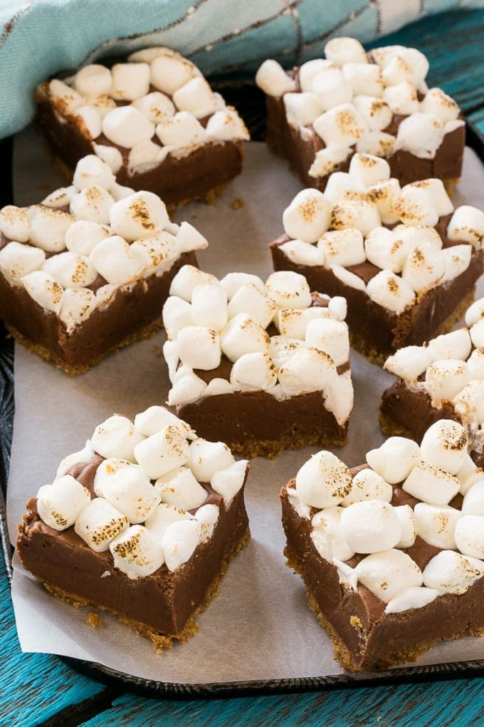Squares of chocolate topped with marshmallows on a parchment lined pan.