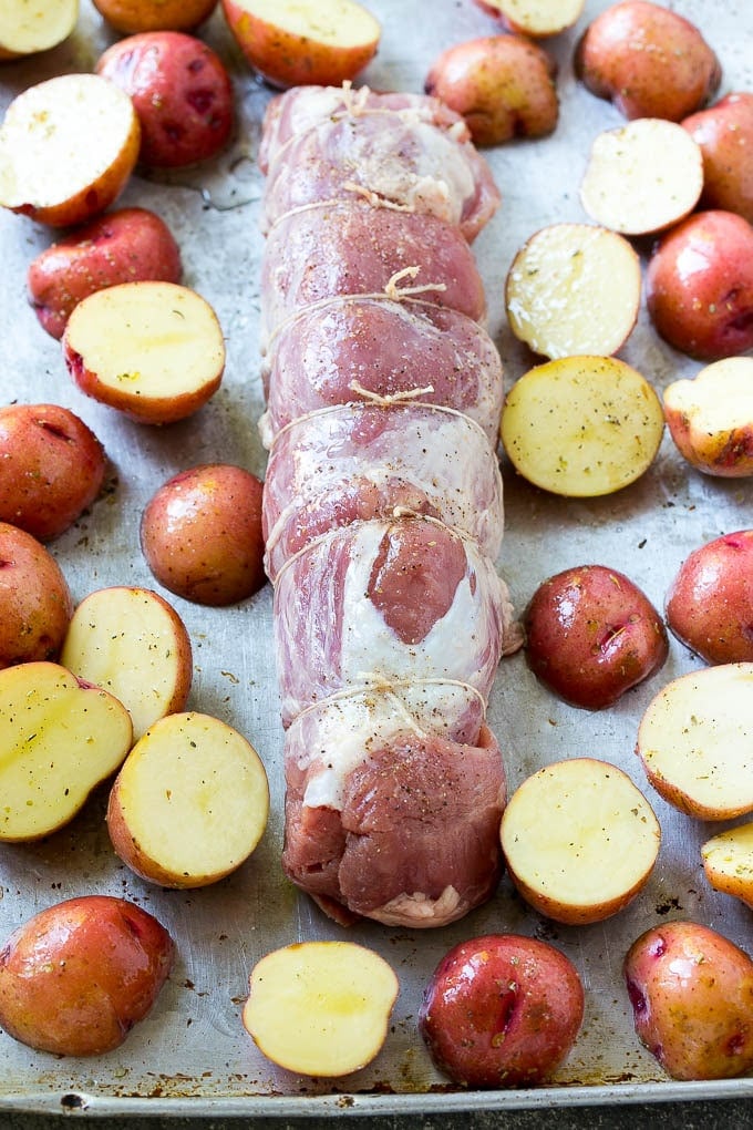 A stuffed pork tenderloin on a baking sheet with halved baby potatoes.
