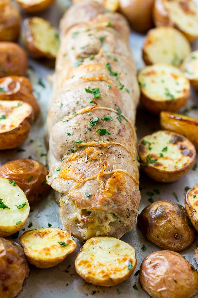 Roasted stuffed pork tenderloin with roasted potatoes on a sheet pan.