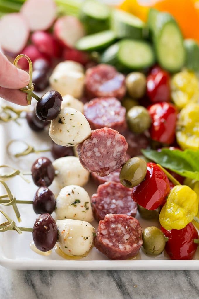 A hand holding up a skewer of salami, cheese and olives.