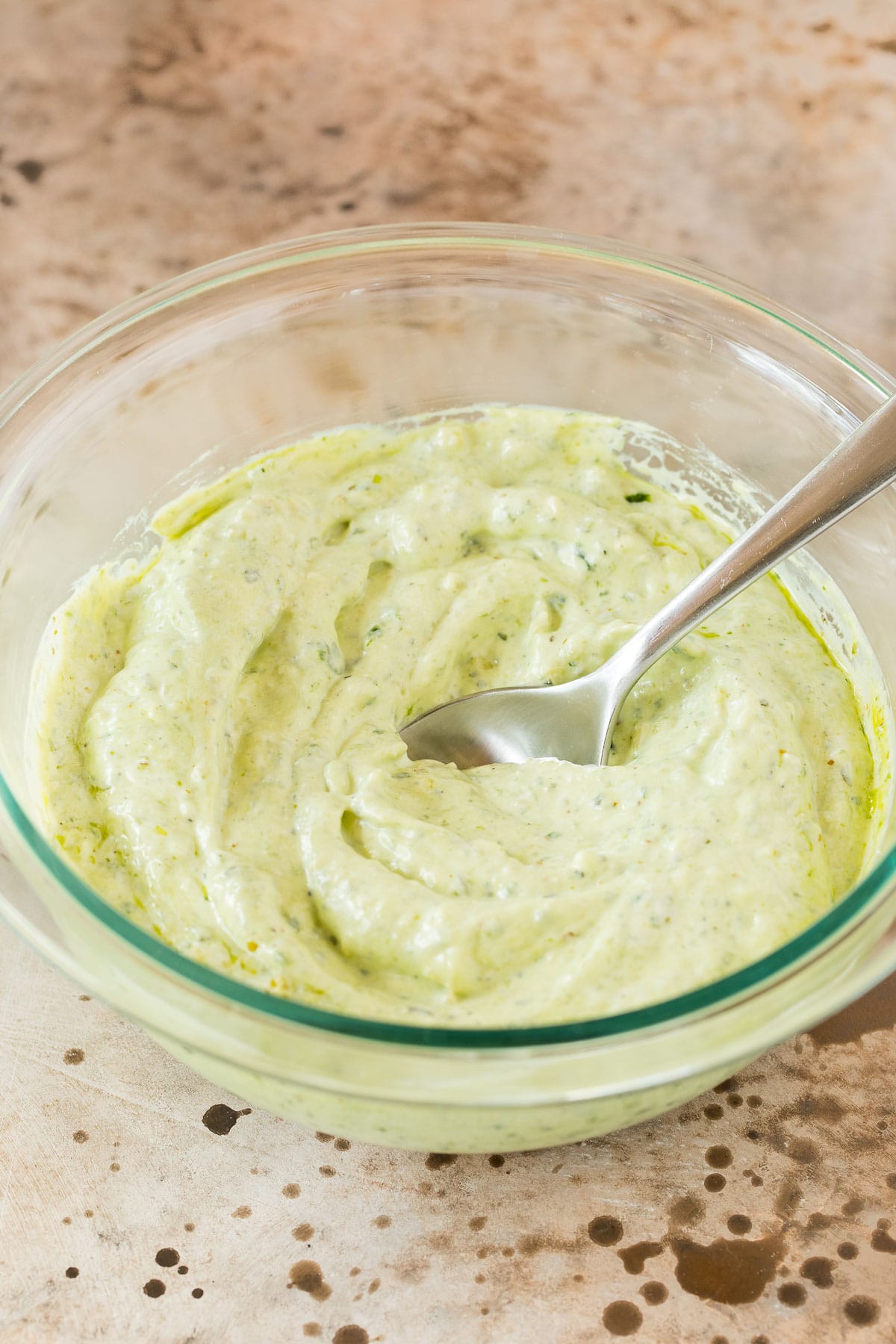 Pesto, mayonnaise and sour cream mixed together in a bowl.