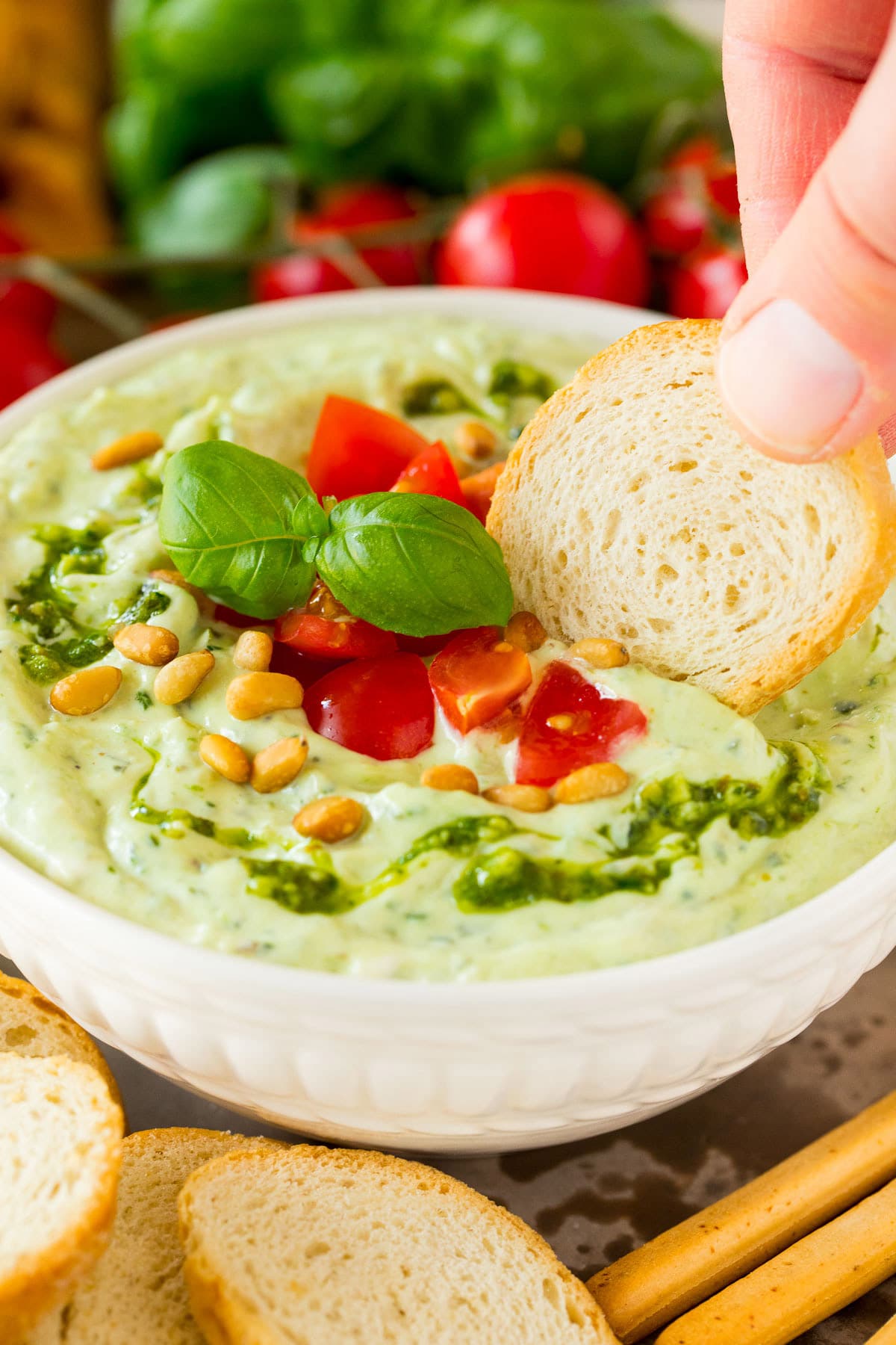 A hand using bread to scoop up pesto dip.