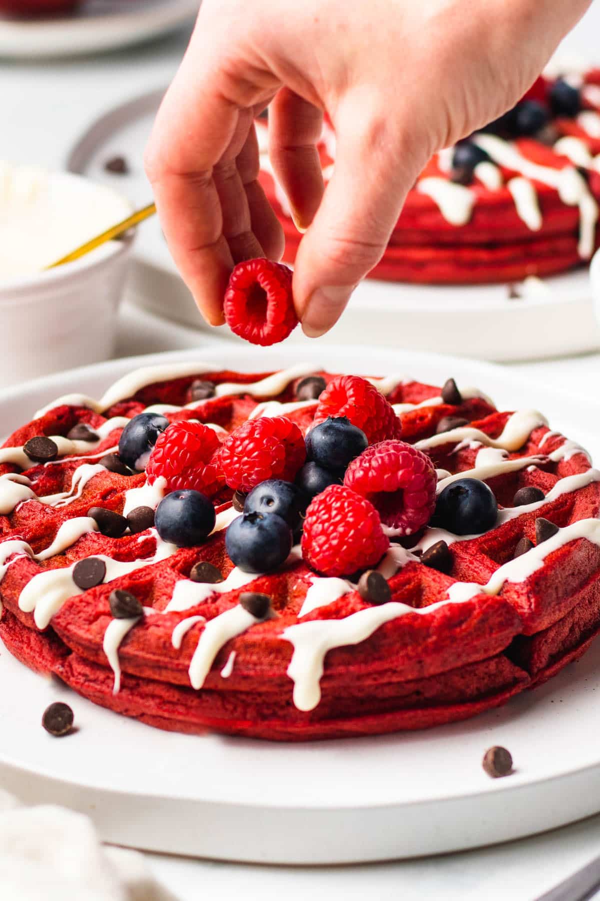 A hand placing berries on top of red velvet waffles.