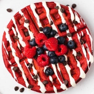 A stack of red velvet waffles topped with cream cheese icing and fresh berries.
