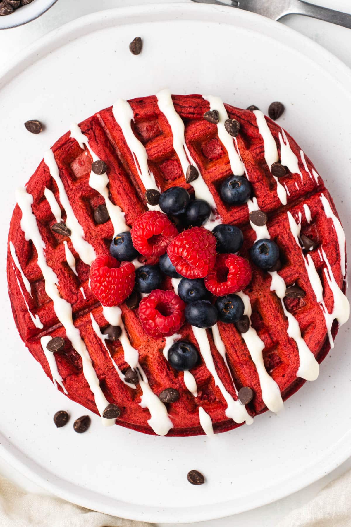 A stack of red velvet waffles topped with cream cheese icing and fresh berries.