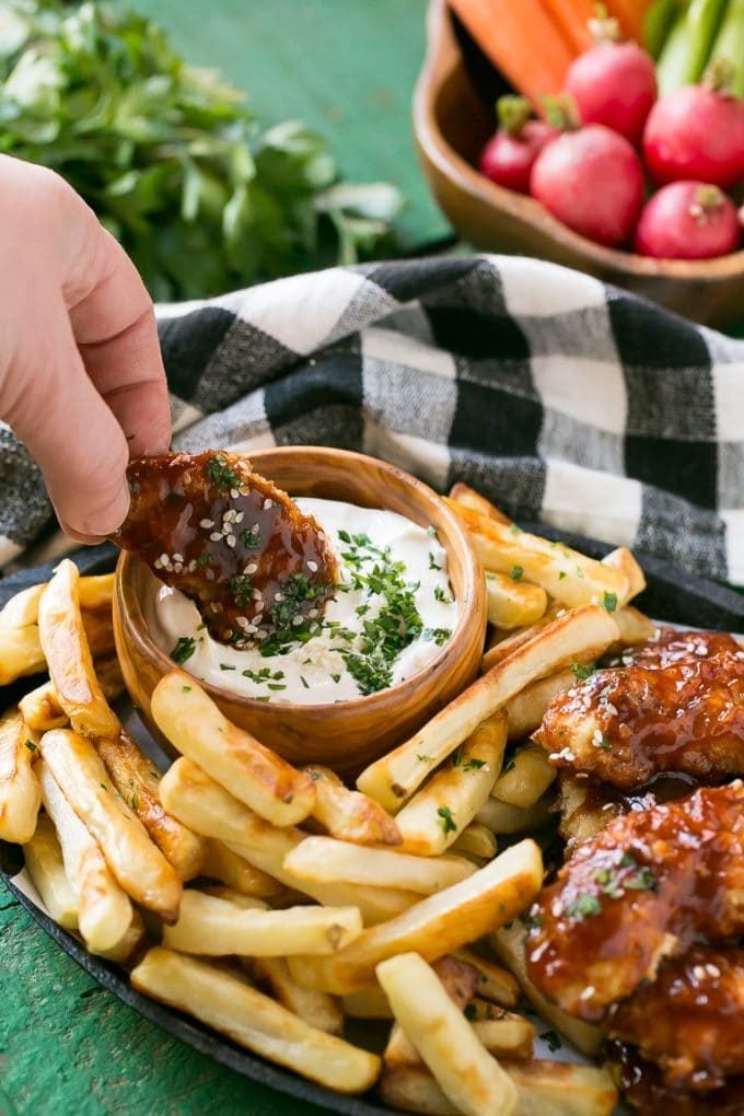 A hand dipping a chicken finger into sauce.