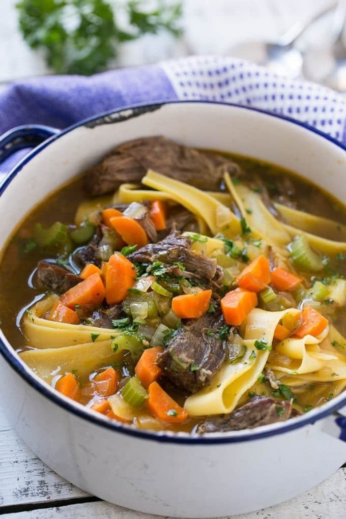 A pot of beef noodle soup with carrots and celery.