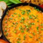 Buffalo ranch chicken dip topped with melted cheese and green onions, surrounded by vegetables, pretzels and baguette slices.