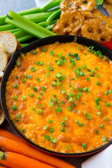 Buffalo ranch chicken dip topped with melted cheese and green onions, surrounded by vegetables, pretzels and baguette slices.