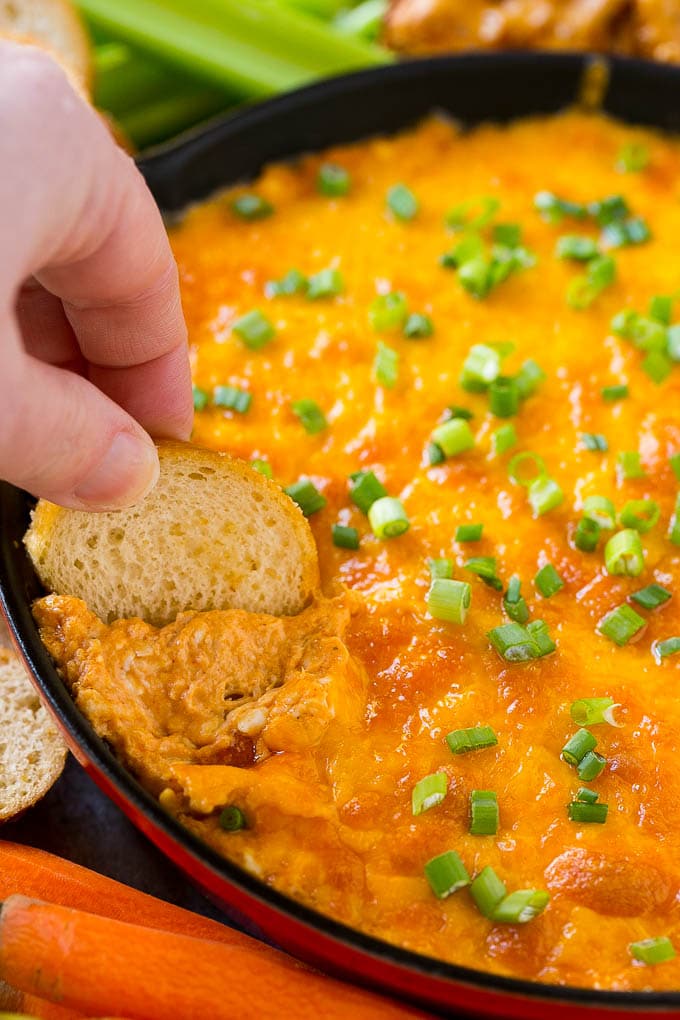 Baked buffalo chicken dip with a baguette slice scooping some out.