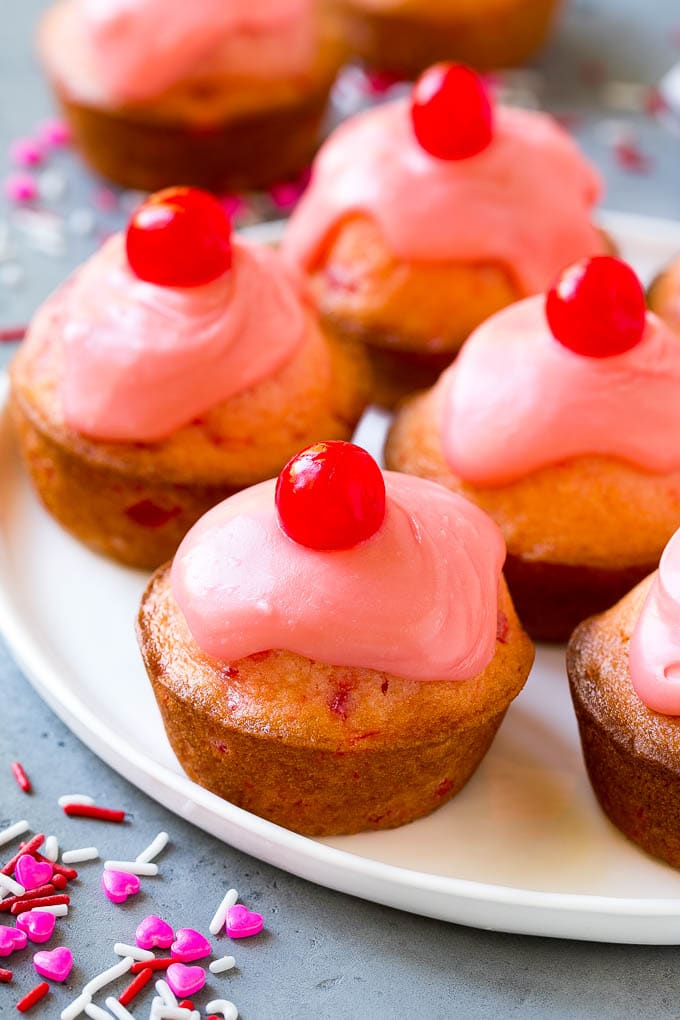 Cherry muffins on a plate, topped with glaze and a whole cherry.