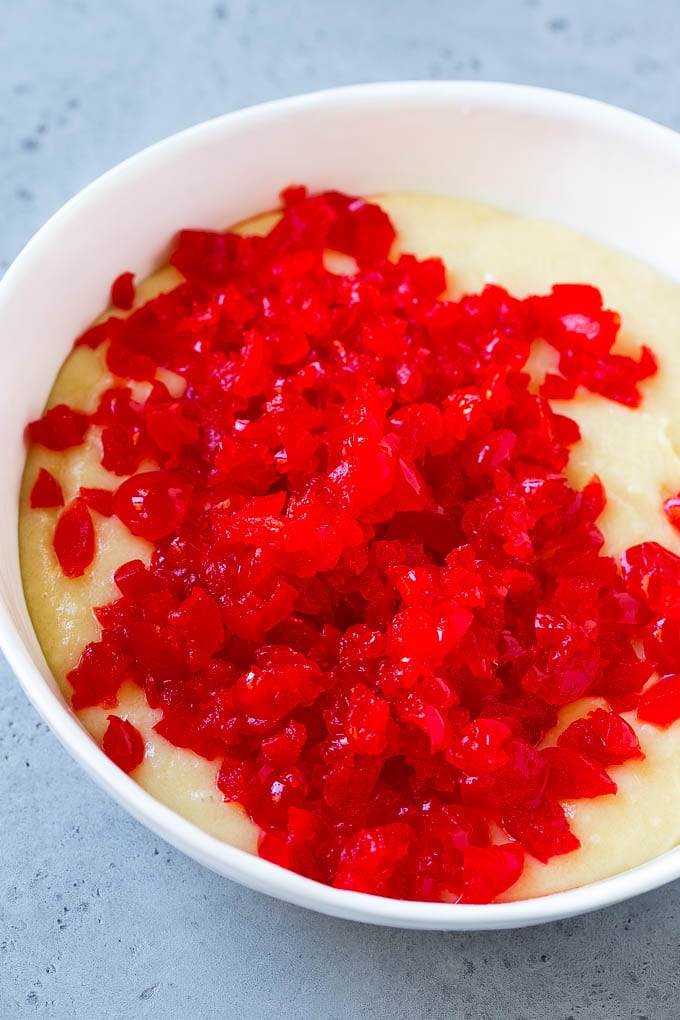 Muffin batter topped with chopped maraschino cherries.