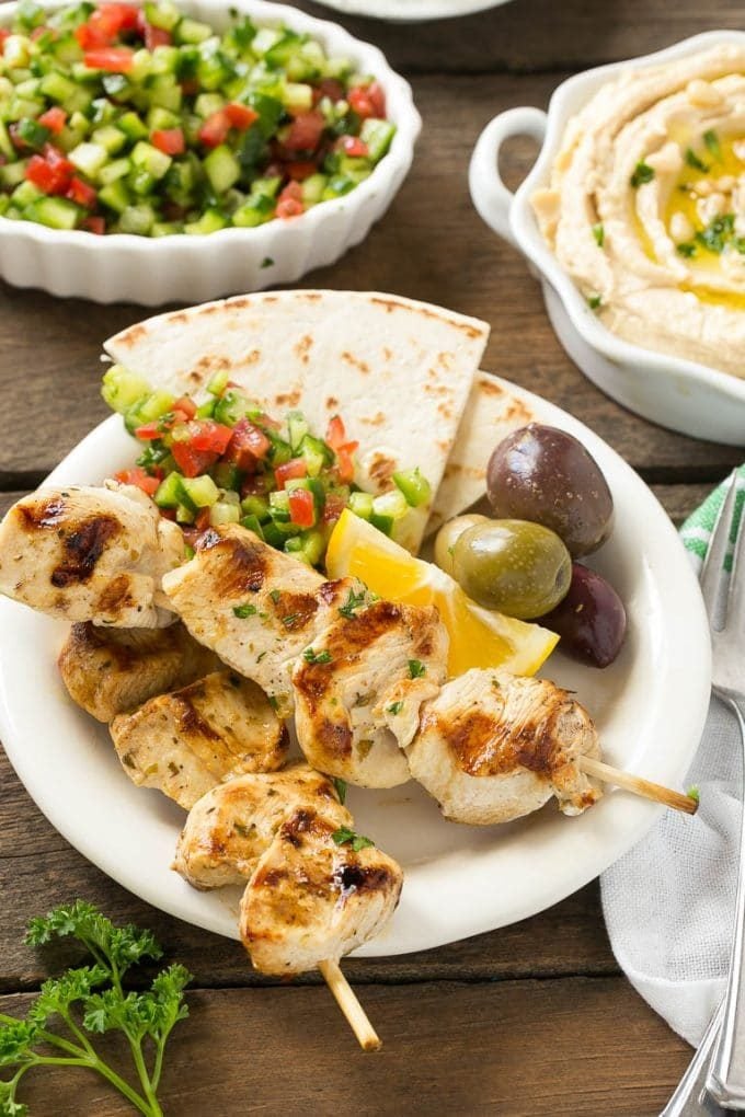 A plate of grilled chicken souvlaki with olives and pita bread.