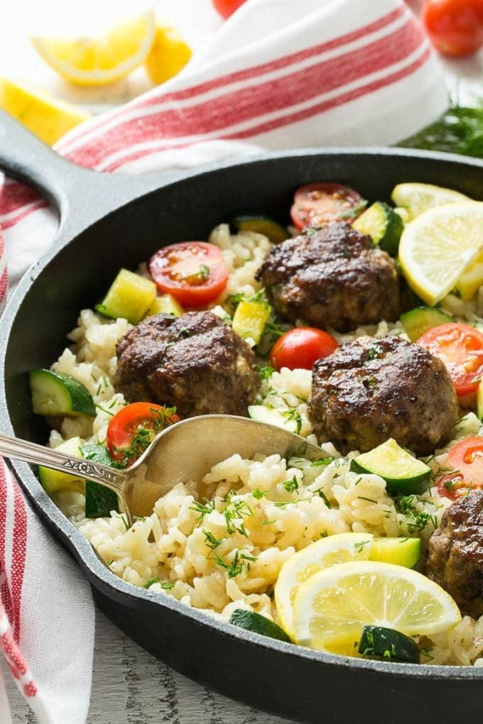 A serving spoon in a dish of meatballs and rice.